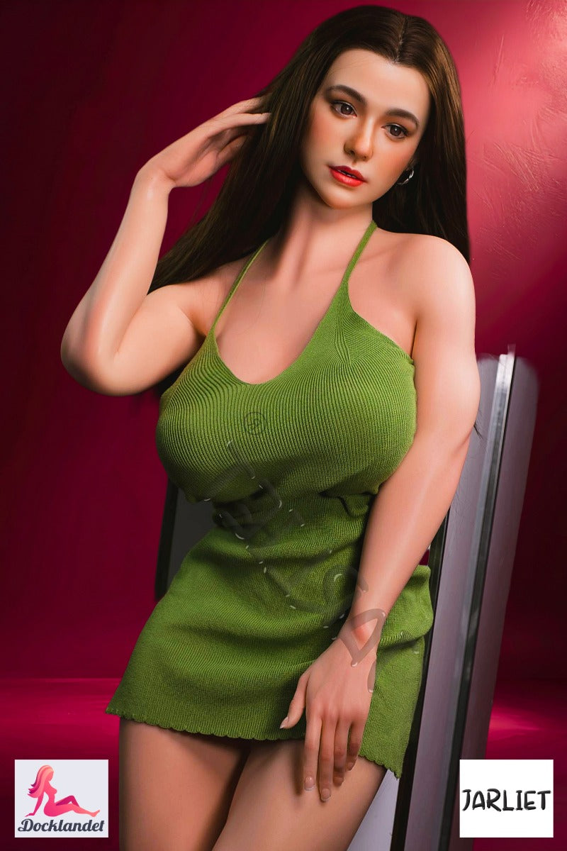 Eve 166 cm silikonsexdocka från Jarliet, står lutad mot piedestal i grön klänning med E-kupa och långt brunt hår mot mörk bakgrund.
